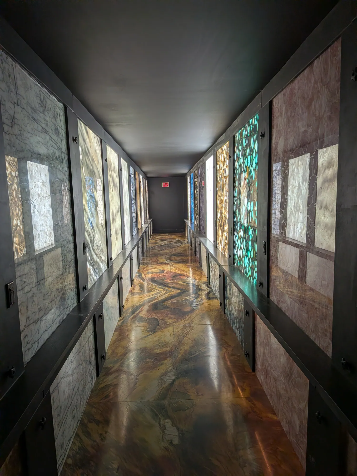 A dark corridor lined with backlit panels of agate and quartz, on a polished stone floor