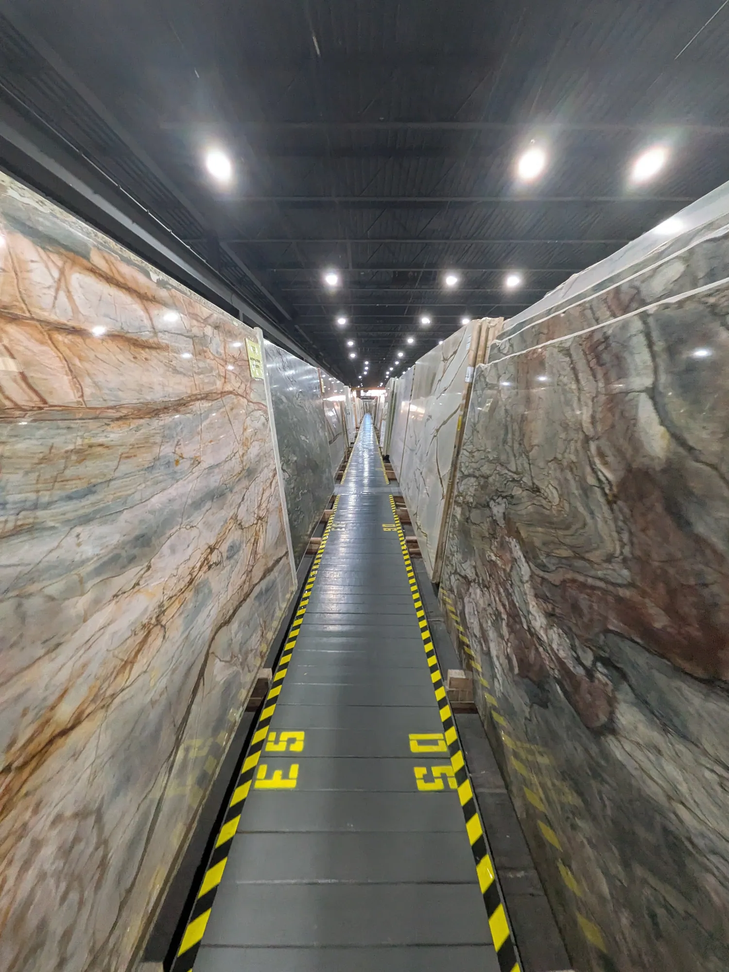 Aisle between a slab with orange-brown veins on a pale ground and a slab in rust, gray and green