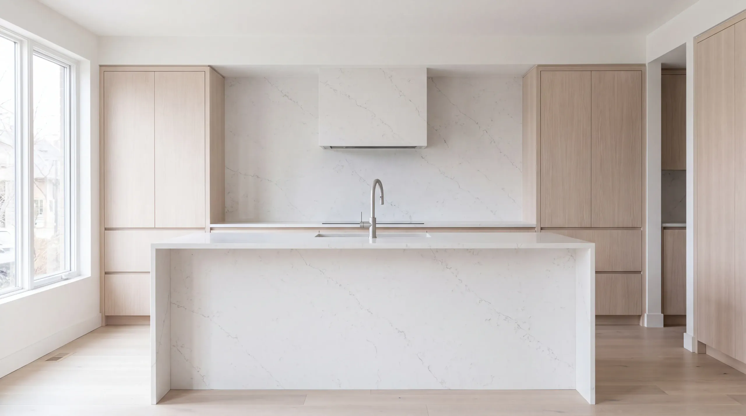 A minimal kitchen with a white quartz waterfall island and backsplash