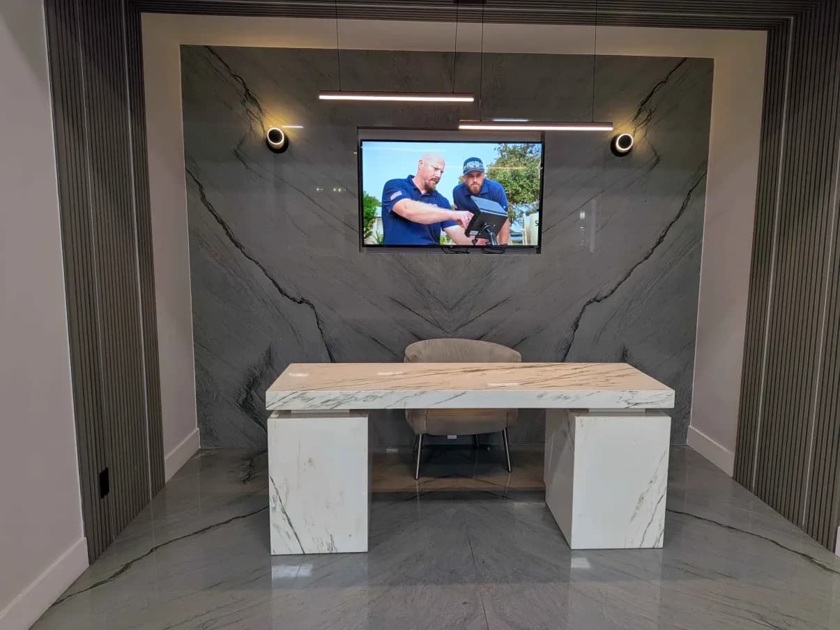 A showroom office set: a white marble waterfall desk in front of a bookmatched gray quartzite feature wall