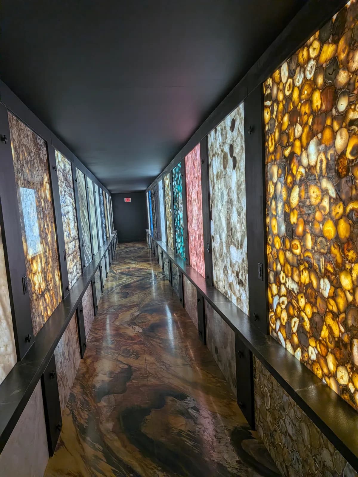 A dark corridor lined with lit panels of agate and quartz, on a polished stone floor