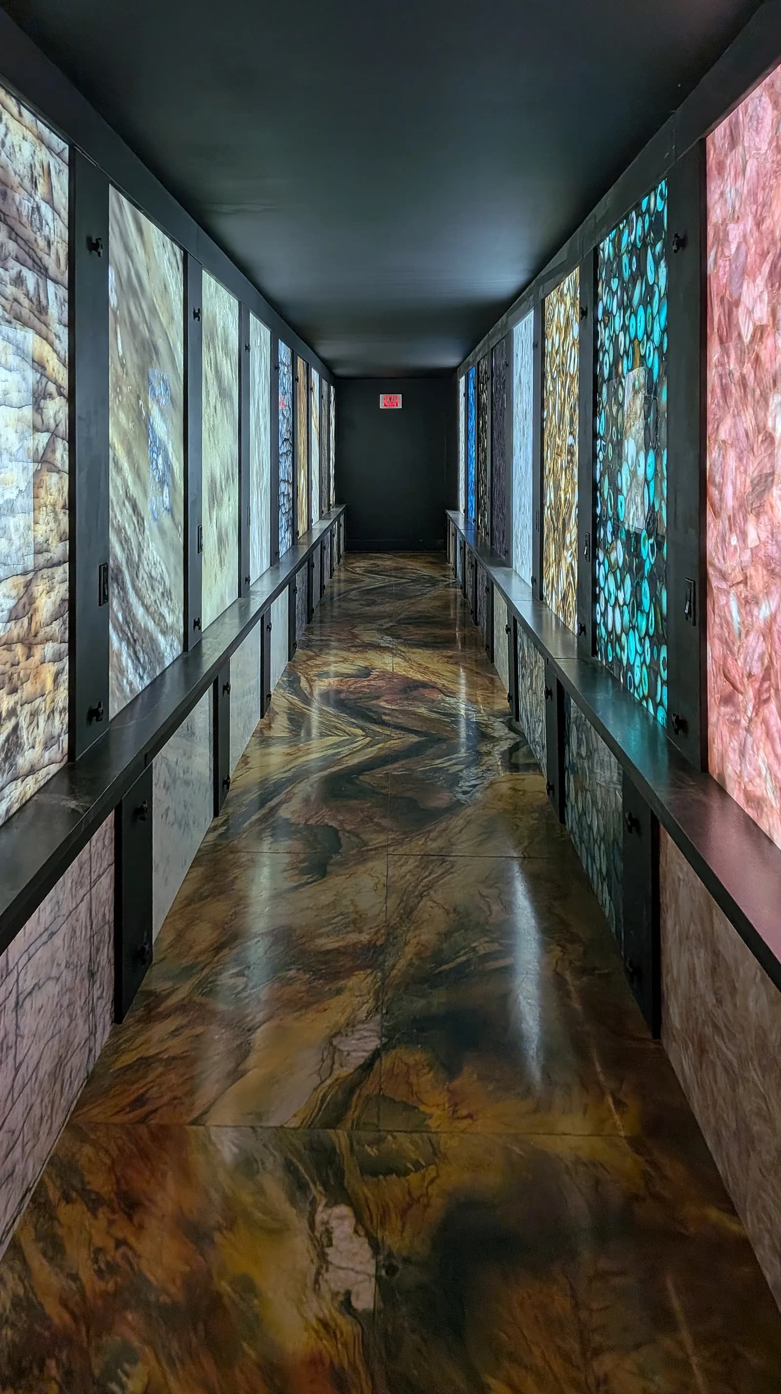 A dark corridor lined with backlit panels of agate and quartz, on a polished stone floor