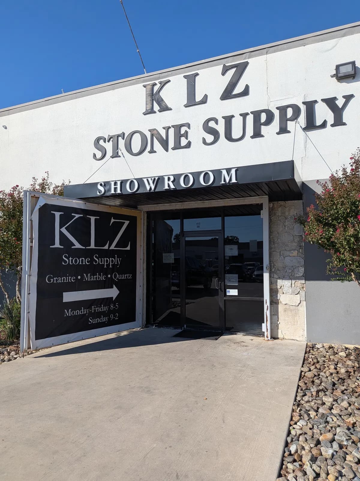 The KLZ Stone Supply showroom entrance in sunlight, with the KLZ sign beside the door