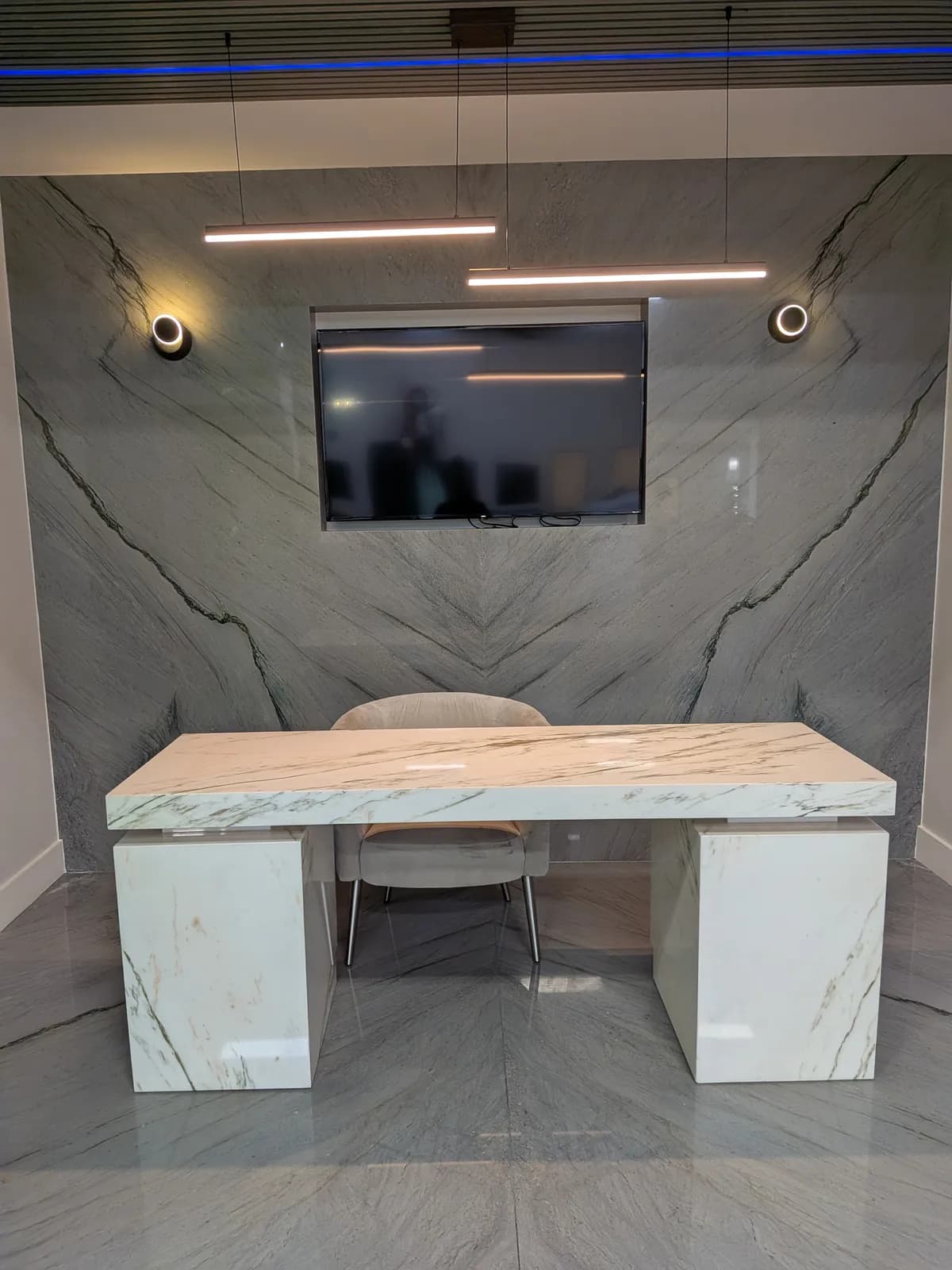 A desk in white veined stone in front of a gray stone feature wall